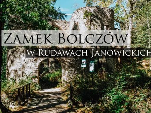 Kamienne ruiny zamku Bolczów w Rudawach Janowickich, porośnięte zielenią, z łukowym wejściem i drewnianym mostkiem.