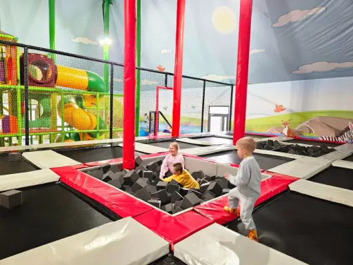 Dzieci bawią się w sławutówko park ewolucji, skacząc na trampolinach i w basenie z gąbkami. Kolorowe zjeżdżalnie i ściany z motywami zwierząt tworzą radosną atmosferę.