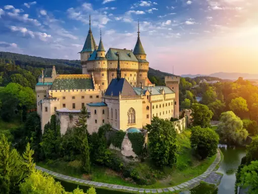 Bajkowy zamek otoczony zielenią, niczym zamek hotel w Polsce, zachwyca o zachodzie słońca.