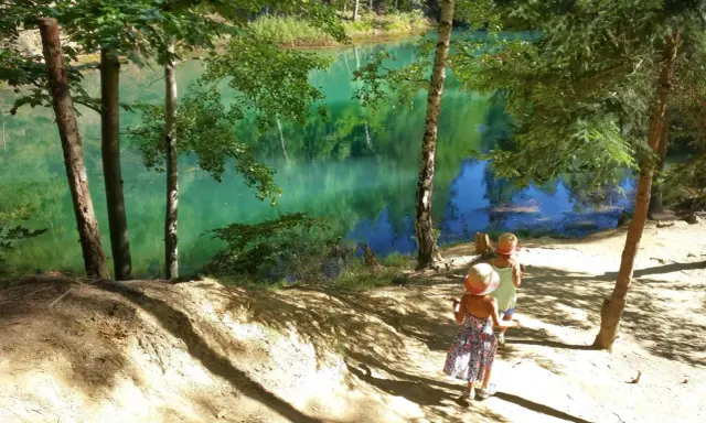 Dwie dziewczynki w słomkowych kapeluszach idą ścieżką nad turkusowe jezioro. Idealne miejsce, gdzie w góry z dzieckiem na spacer.