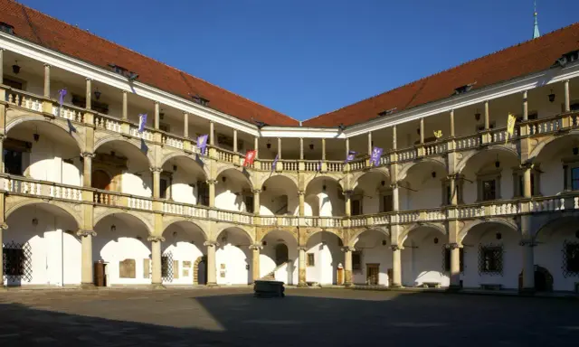 Dziedziniec zamku w Brzegu z arkadowymi krużgankami, kolumnami i flagami. Zamek w Brzegu ciekawostki – piękna renesansowa architektura.
