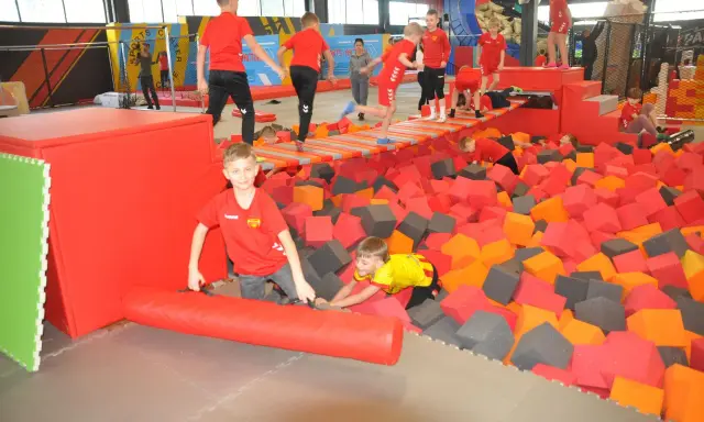 Dzieci bawią się w basenie z gąbkami w Flypark Kielce. Jeden chłopiec w czerwonej koszulce próbuje wstać, a drugi w żółtej wspina się po gąbkach.