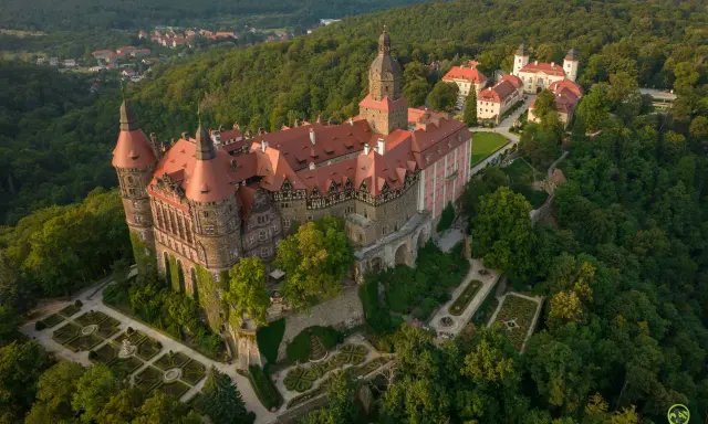 Zamek Książ otoczony zielenią, z widokiem na okoliczne wzgórza i miasteczko.