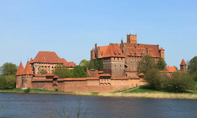 Potężne ceglane zamki na Mazurach, z czerwonymi dachami i wieżami, górują nad spokojną wodą.