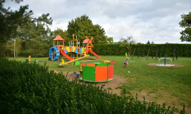 Kolorowy plac zabaw z karuzelą i huśtawkami, idealny dla dzieci odwiedzających farmę strusi Kniewo.