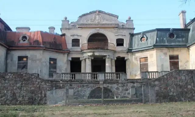 Opuszczony pałac w Bratoszewicach, zniszczony, z zabitymi deskami oknami i zardzewiałą balustradą.