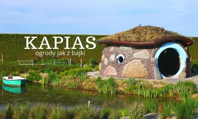 Bajkowy domek z kamienia i cegły, porośnięty trawą dach, otoczony zielenią i stawem. Ciekawe ogrody jak z bajki.