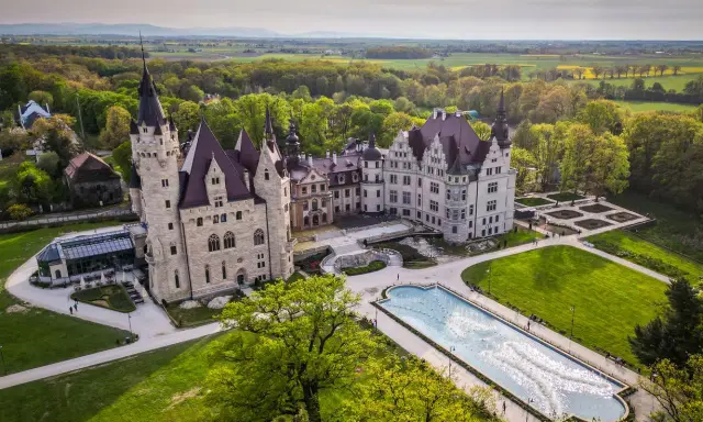 Majestatyczny pałac, największy w Polsce, otoczony zielenią i ogrodem z fontanną.