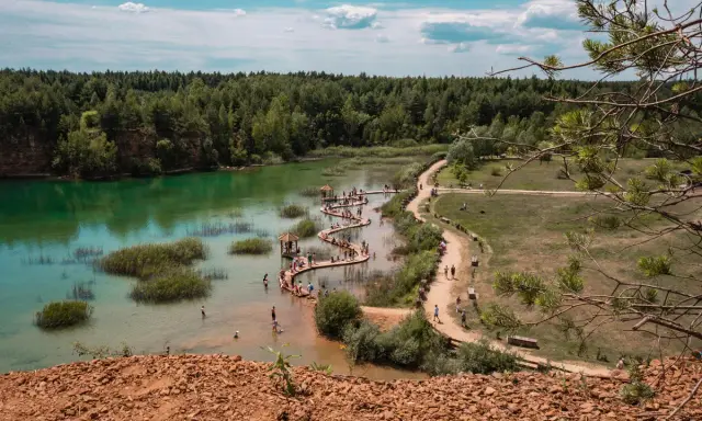 Polskie Malediwy, gdzie można się kąpać. Turkusowa woda, drewniane molo wijące się po jeziorze, otoczone lasem. Ludzie odpoczywają i kąpią się.