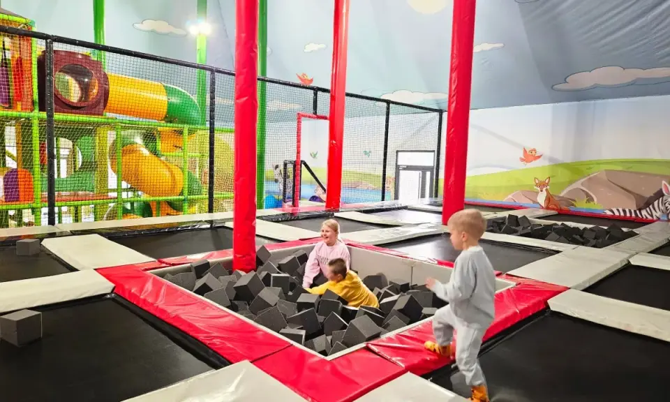 Dzieci bawią się w sławutówko park ewolucji, skacząc na trampolinach i w basenie z gąbkami. Kolorowe zjeżdżalnie i ściany z motywami zwierząt tworzą radosną atmosferę.