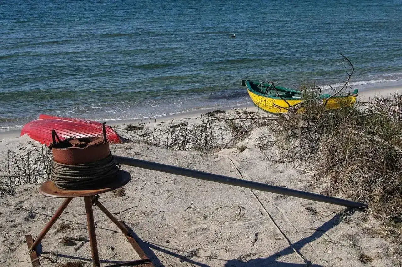 Na plaży w Polsce leżą dwie łodzie: czerwona i ż&oacute;łta. W tle widać morze.