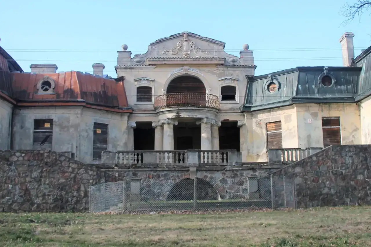 Opuszczony pałac w Bratoszewicach, zniszczony balkon i okna, kamienne mury i zardzewiała balustrada.