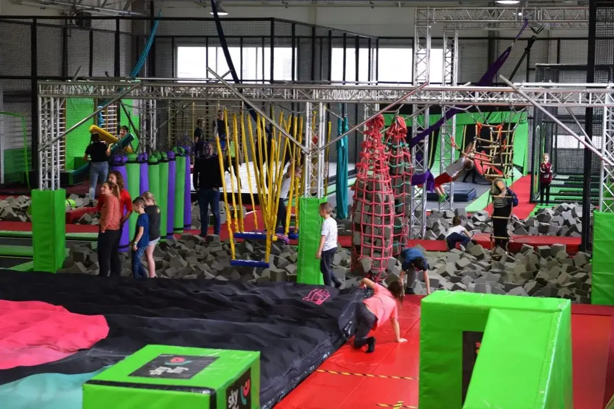 Dzieci bawią się na torze przeszkód w Flypark Kielce, skacząc i wspinając się wśród piankowych kostek i lin.