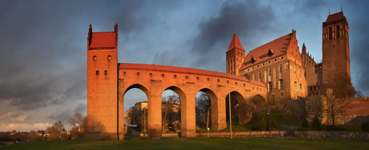 Imponujące zamki na Pomorzu, z ceglanymi murami i czerwonymi dachami, oświetlone zachodzącym słońcem.