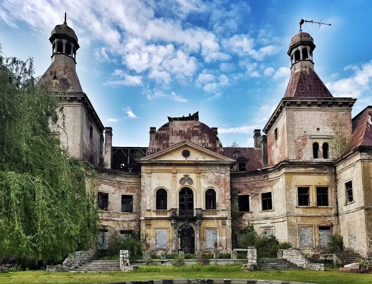 Opuszczony pałac Mańczyce, zniszczony, z wieżami i zrujnowanym dachem, pod błękitnym niebem z chmurami.