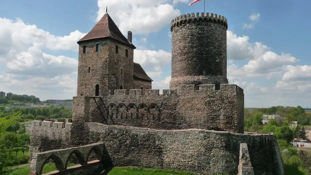 Kamienny zamek w Będzinie, z okrągłą wieżą i polską flagą, skrywa wiele ciekawostek.