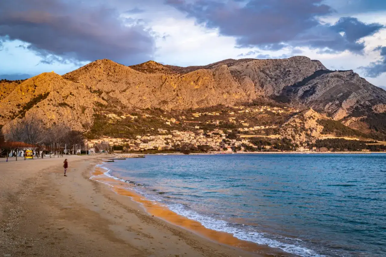 Plaża w Omiś, z g&oacute;rami w tle i miasteczkiem na zboczu. Idealne miejsce na relaks i odkrywanie atrakcji.