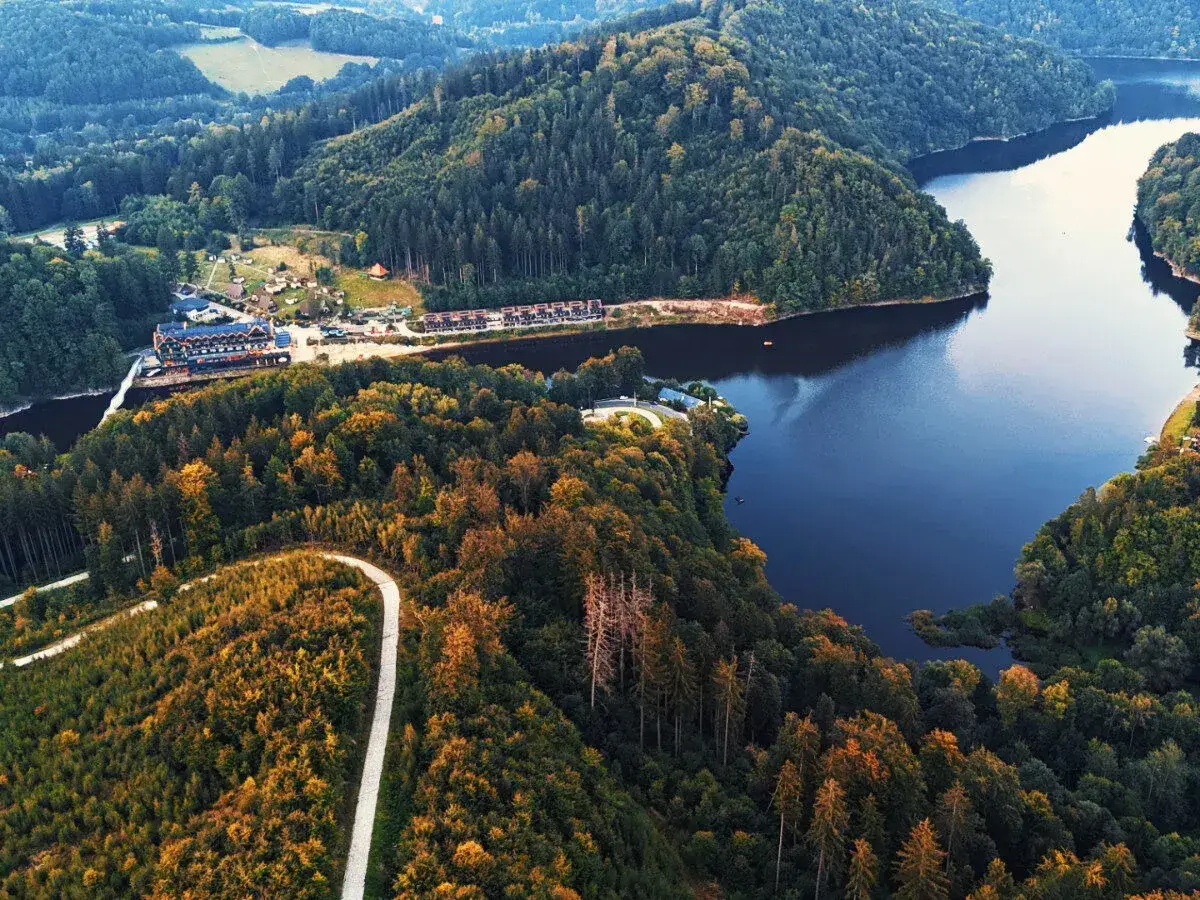 Malownicze zbiorniki wodne Dolny Śląsk otoczone jesiennymi lasami. Widok z lotu ptaka na hotel i drogę wijącą się wśród drzew.