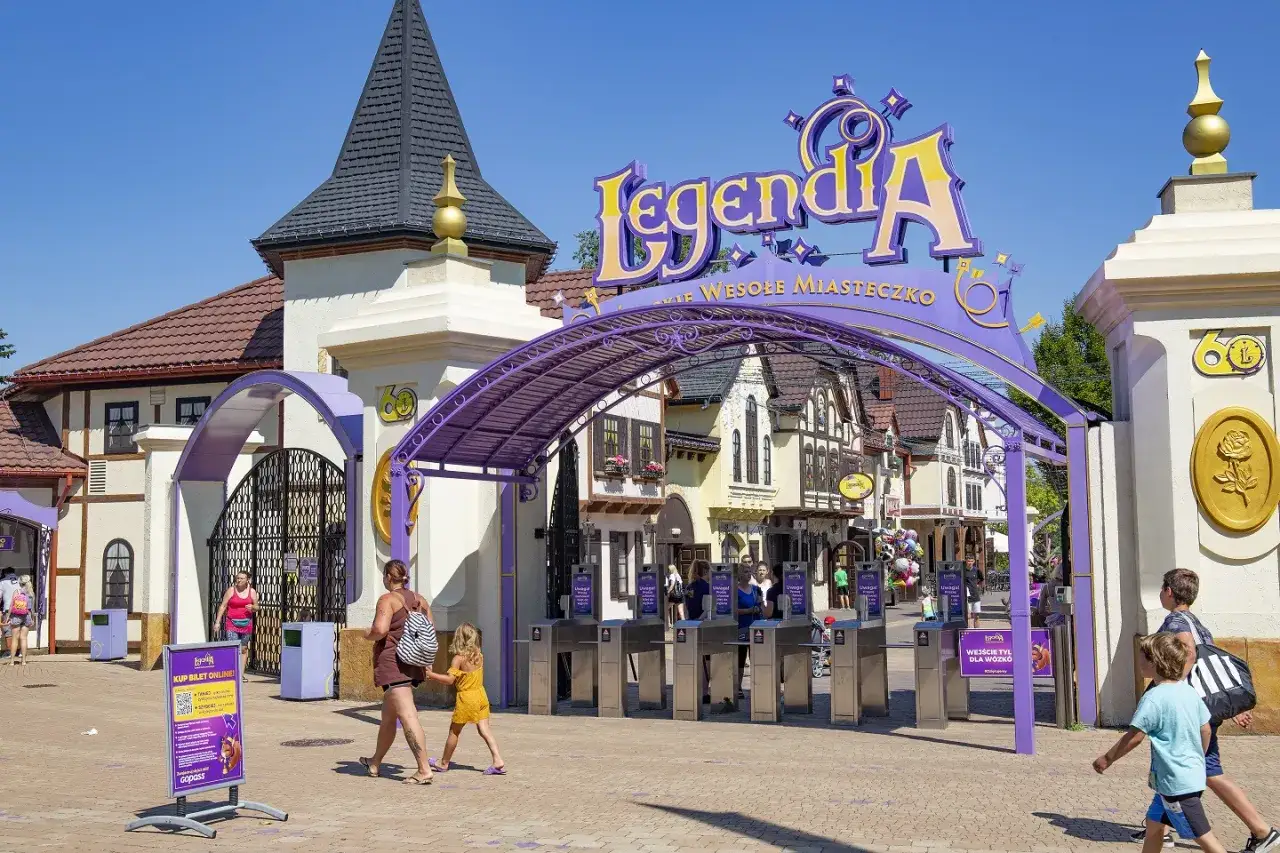 Wejście do Legendii, wesołego miasteczka w Chorzowie. Rodziny wchodzą przez bramki pod fioletową konstrukcją z napisem.