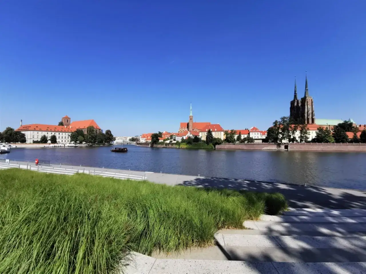 Wrocławski widok na Ostrów Tumski i rzekę. Idealne miejsce, gdzie na spacer we Wrocławiu, z trawą i schodami w pierwszym planie.