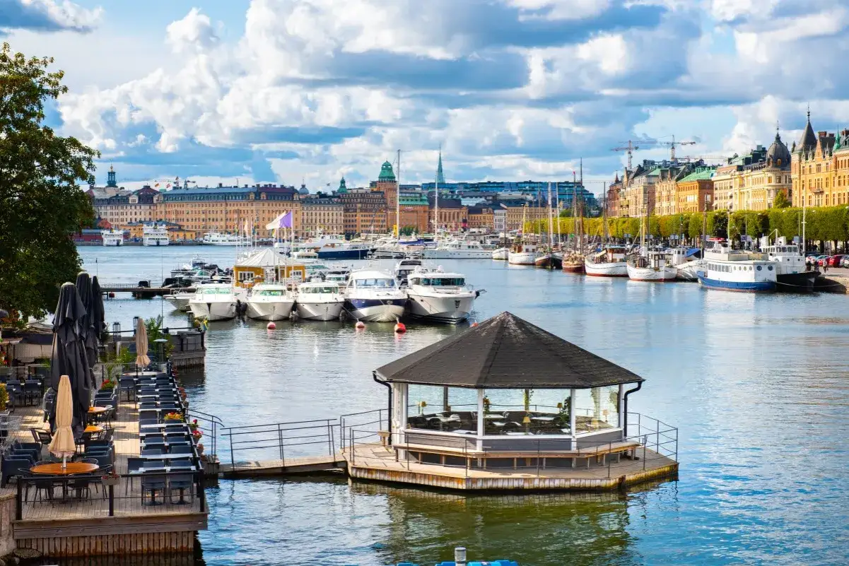 Idealny weekend w Szwecji: malowniczy port z łodziami, urokliwa restauracja na wodzie i zabytkowa zabudowa miasta w tle.