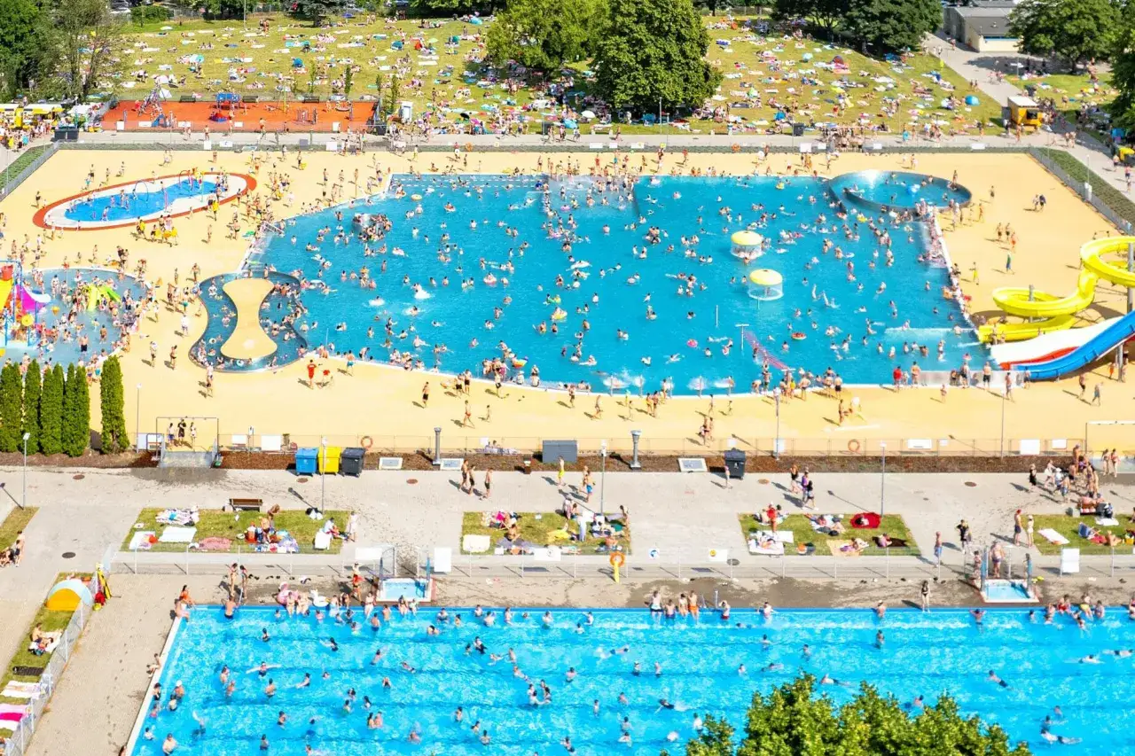 Tłum ludzi cieszy się słońcem i wodą w Moczydło water park. Wodne atrakcje, baseny i zjeżdżalnie przyciągają tłumy.